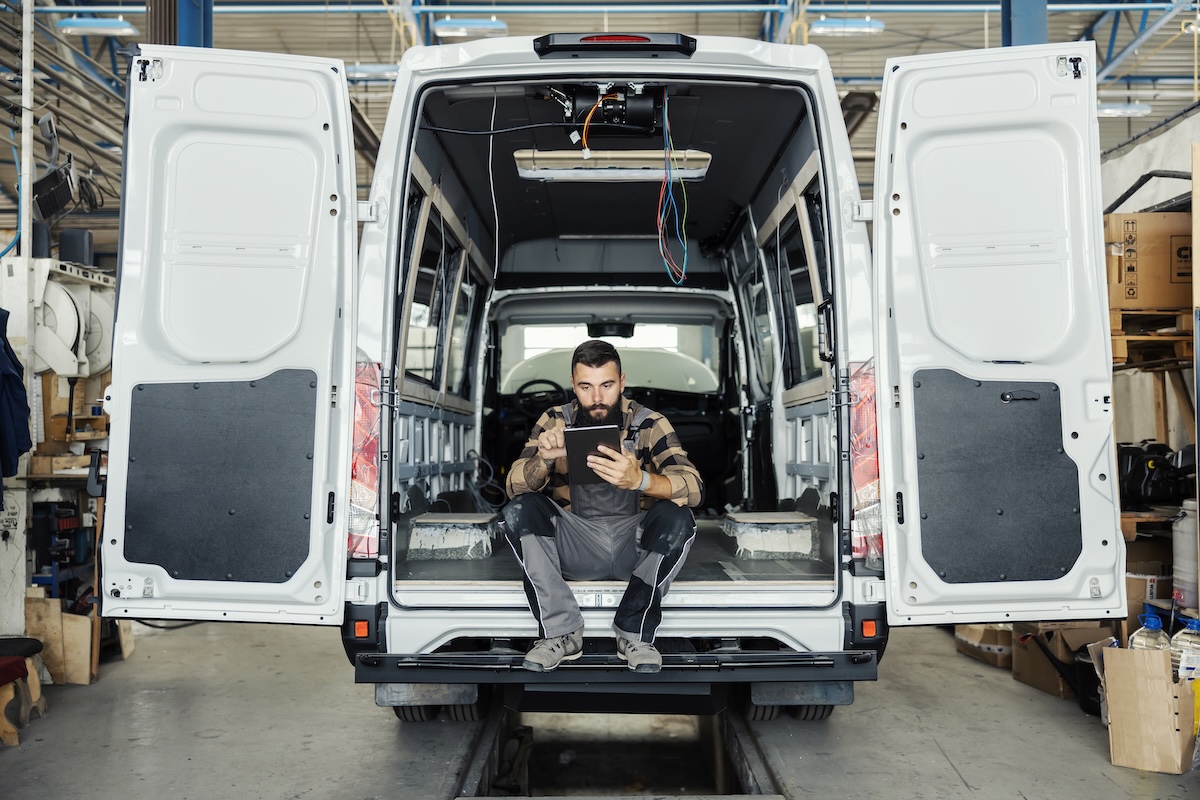 Technician sitting in maintenance HVAC plumbing van using a mobile tablet.