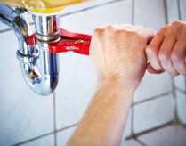 Hands using a wrench to tighten an under-sink pipe