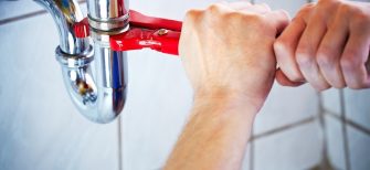 Hands using a wrench to tighten an under-sink pipe