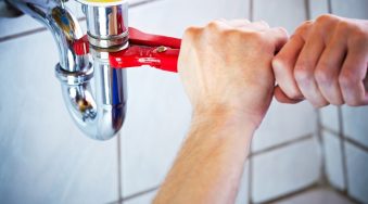 Hands using a wrench to tighten an under-sink pipe