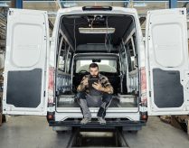 Technician sitting in maintenance HVAC plumbing van using a mobile tablet.