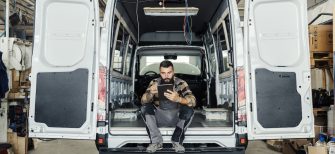Technician sitting in maintenance HVAC plumbing van using a mobile tablet.