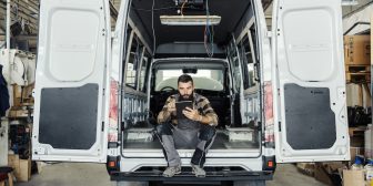 Technician sitting in maintenance HVAC plumbing van using a mobile tablet.