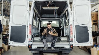 Technician sitting in maintenance HVAC plumbing van using a mobile tablet.