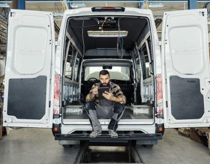 Technician sitting in maintenance HVAC plumbing van using a mobile tablet.
