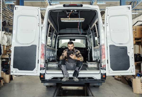 Technician sitting in maintenance HVAC plumbing van using a mobile tablet.