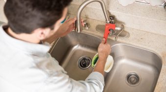 Male plumber using a wrench to tighten a water faucet in a kitchen, seen up close